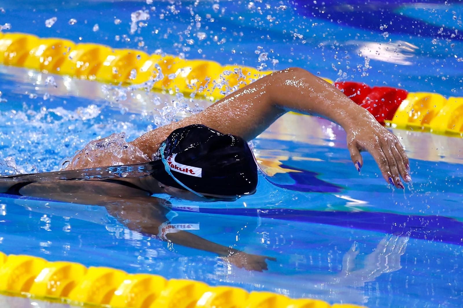 Swimmer in black cap performing freestyle stroke in a pool with yellow lane dividers.