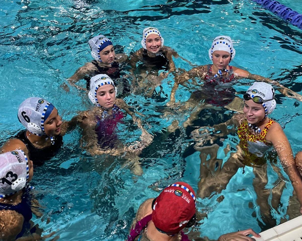 Group of water polo players in a pool wearing caps, gathered for a huddle or discussion.